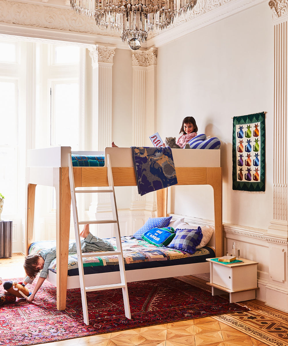Children in a room with a bunk bed; one reads on the top, another plays below, with colorful decor and a Funny Face Pillow contributing to the vibrant ambiance.