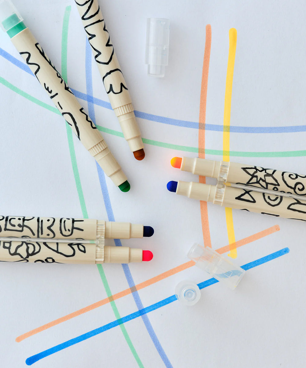 Five Le Well Rounded Markers with black-patterned barrels are lying on paper covered in colorful lines.