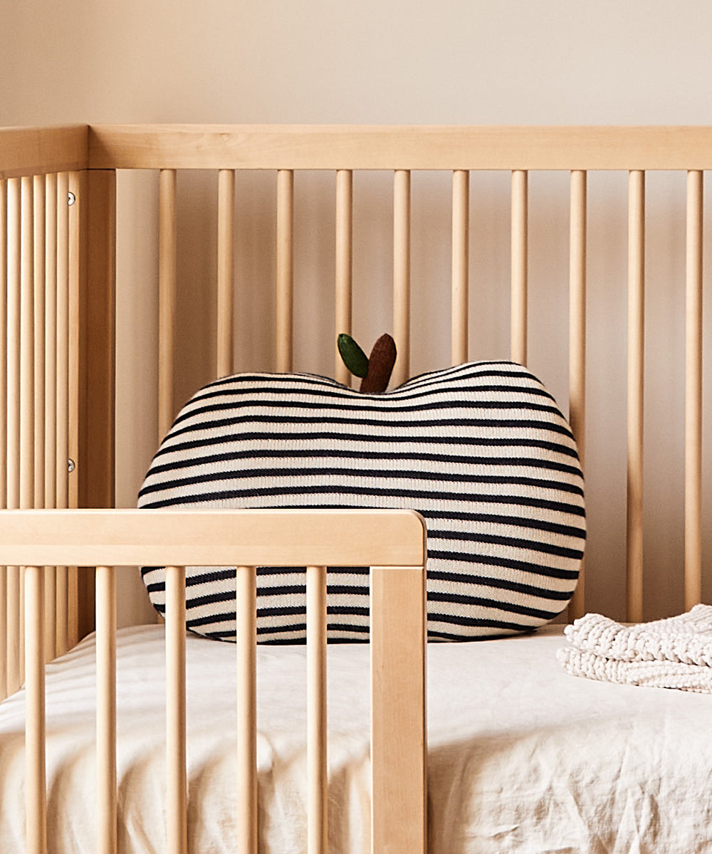 Apple Pillow in a wooden crib with a beige blanket.