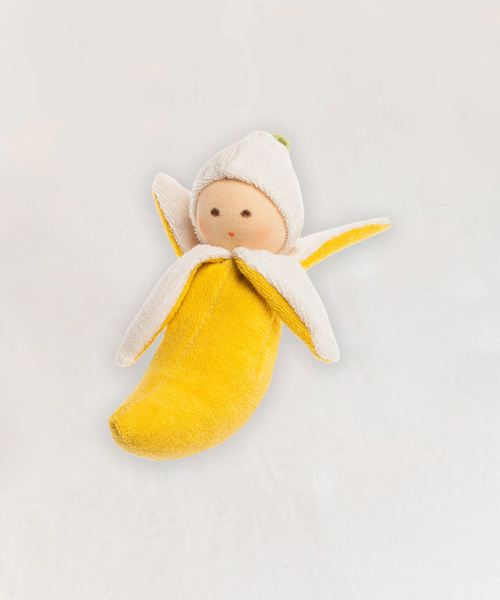 The Banana Rattle is a soft doll with a banana-shaped body and fabric face, wrapped in a peeled banana costume.