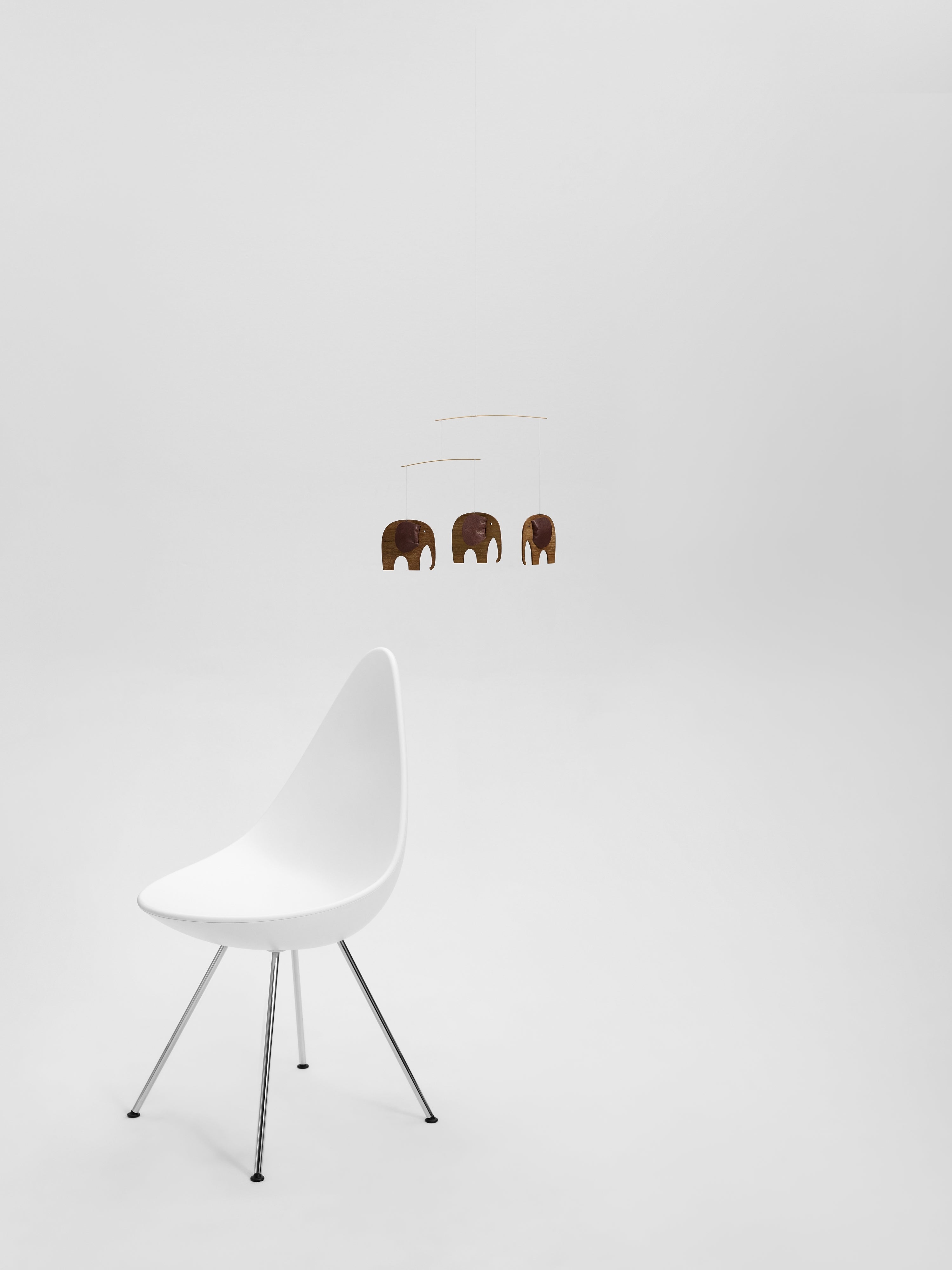 A white chair on a white floor with a Baby Elephants 3 | Wood mobile featuring three brown elephants hanging in the background.