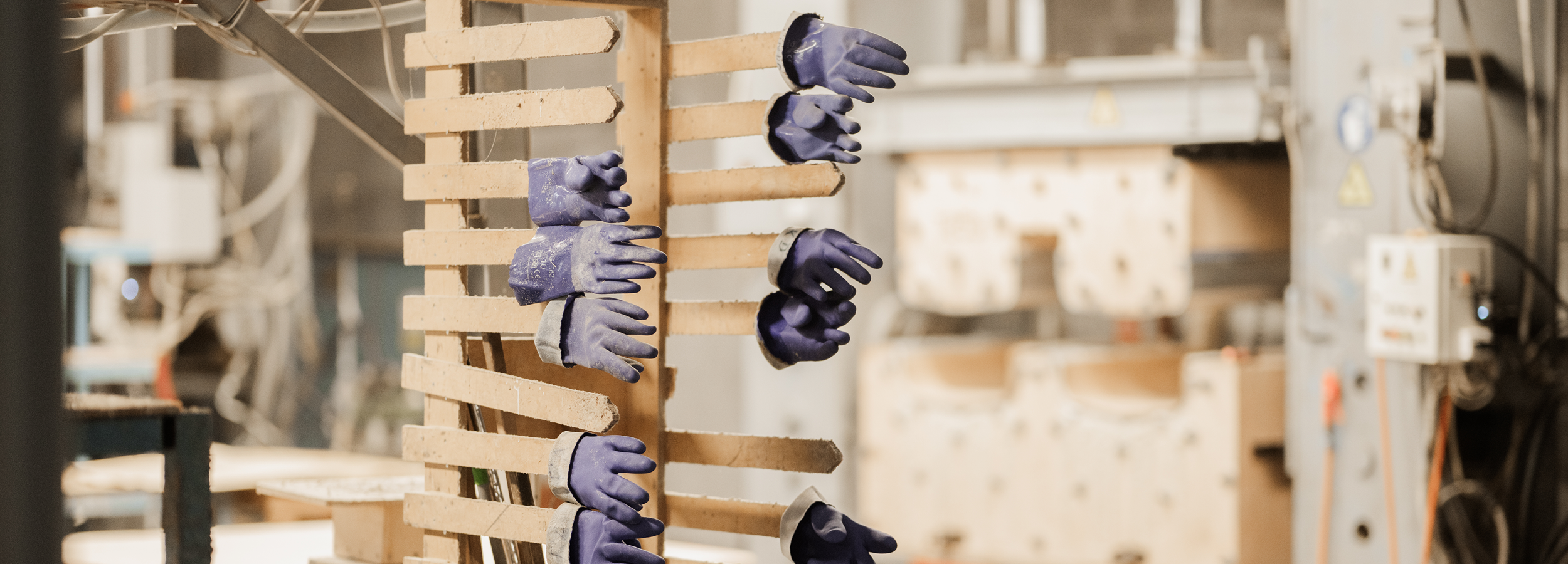 Conveyor with drying racks holding multiple blue rubber gloves in a factory setting.