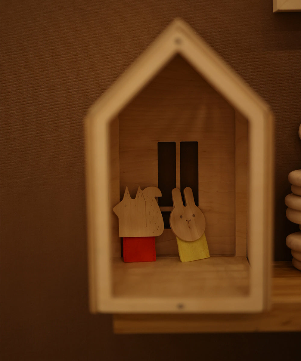 A wooden house-shaped shelf featuring two animal figurines, a fox and a rabbit, each on colored bases.