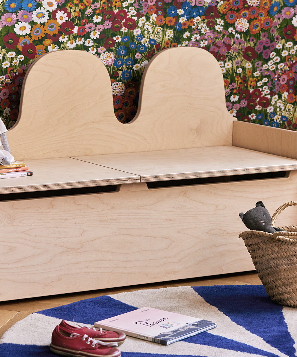 Wooden bench with storage compartment against a floral wall.