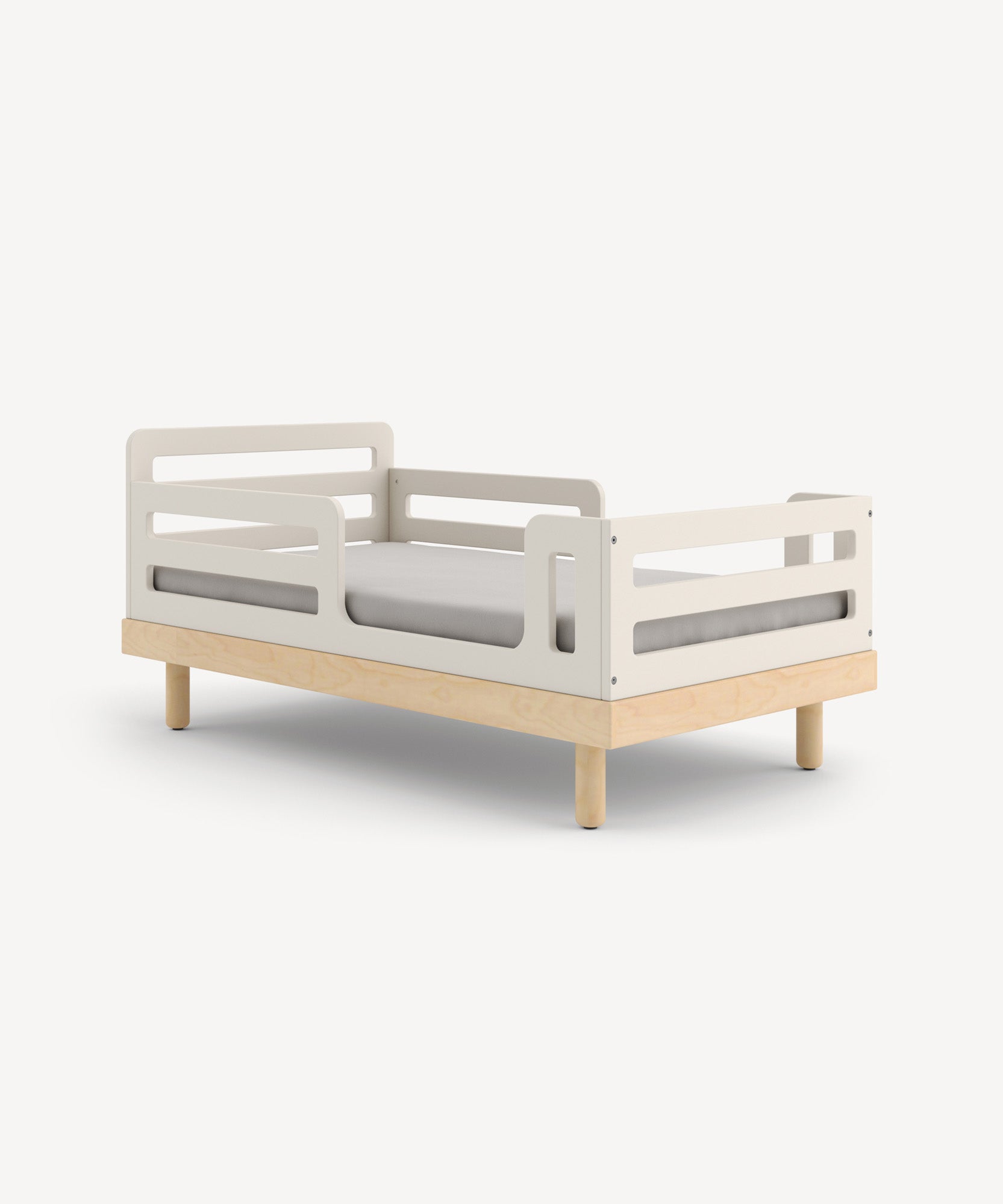 The Classic/Arbor Toddler Bed Conversion Kit is a minimalist child’s bed with a light wood frame, gray mattress, and protective side rails.