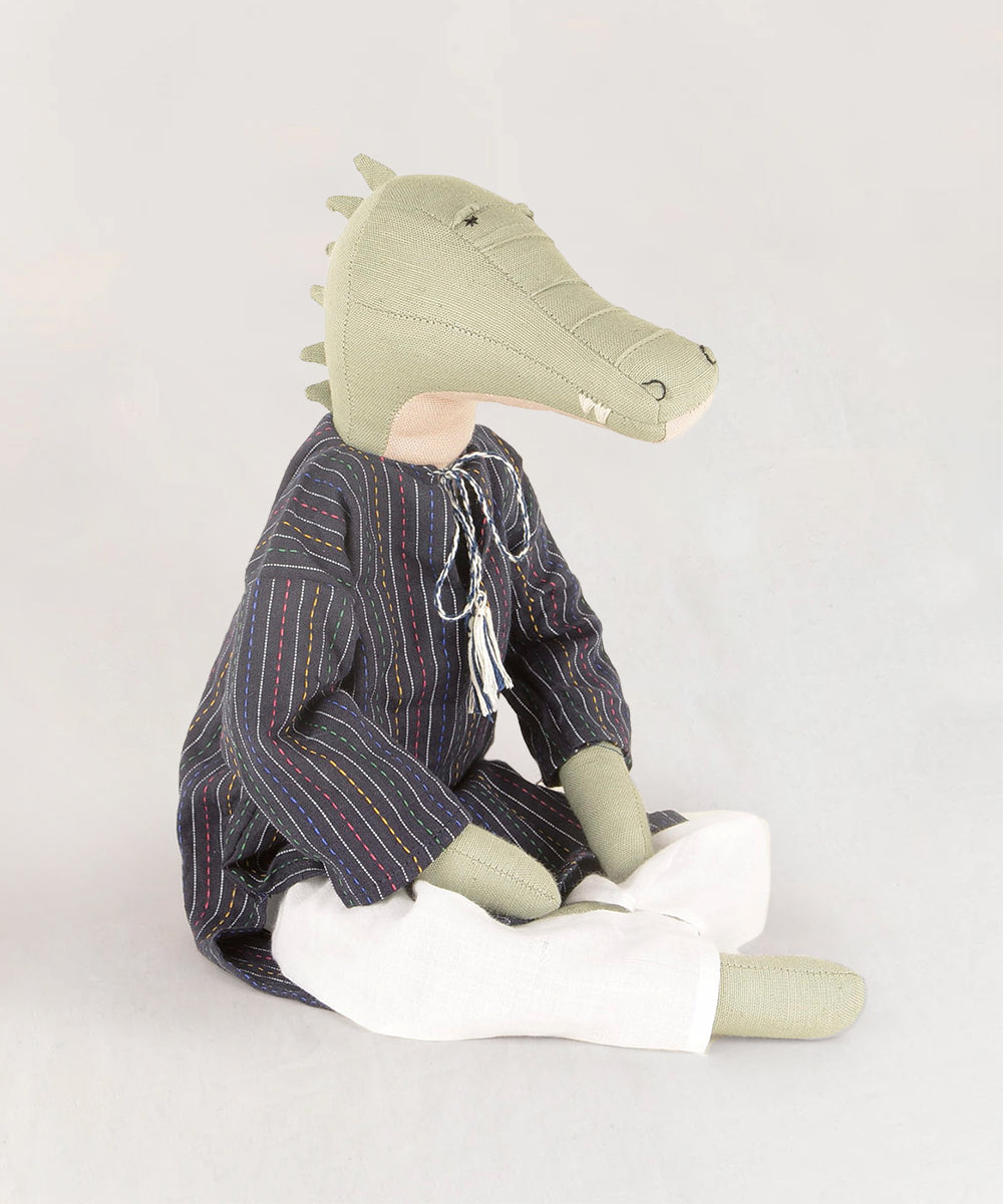 Le Crocodile: a stuffed crocodile toy wearing a striped shirt and white pants while sitting.