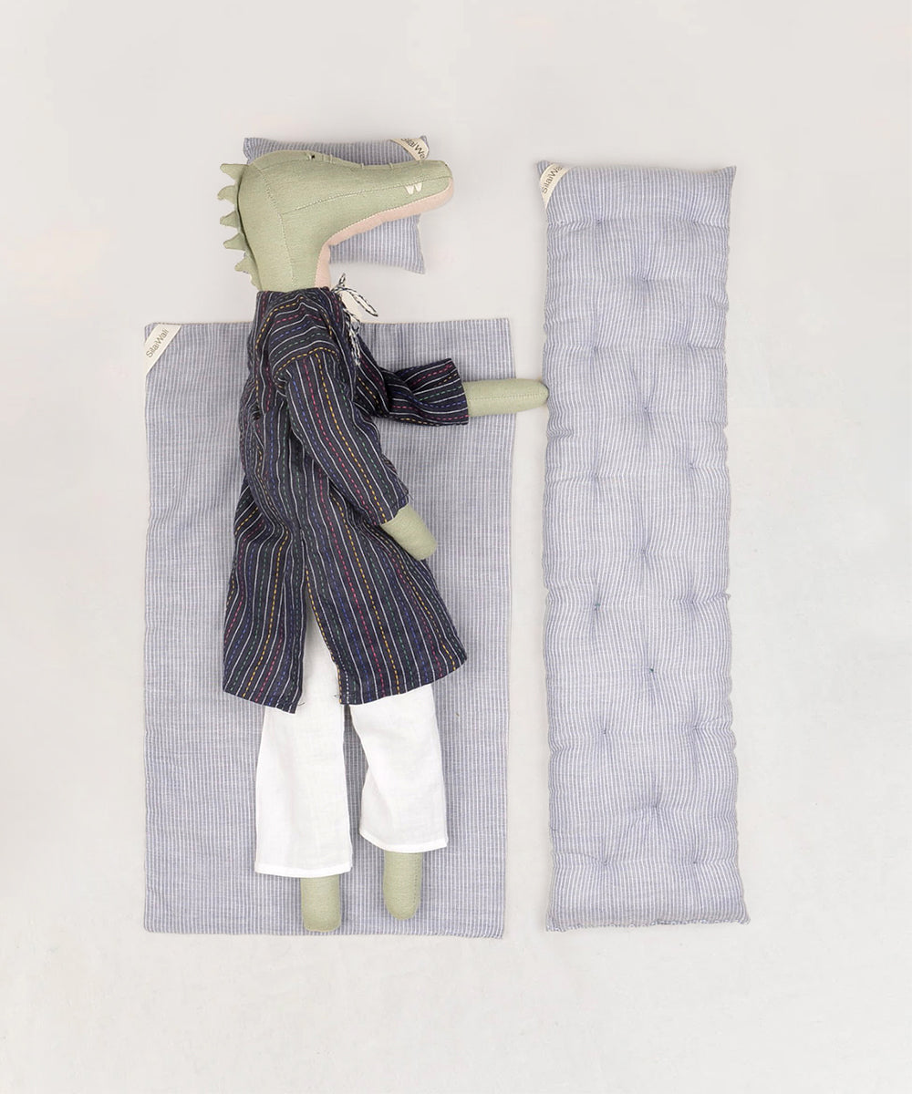 Le Crocodile plush toy in pajamas rests on a striped mat with a small pillow.