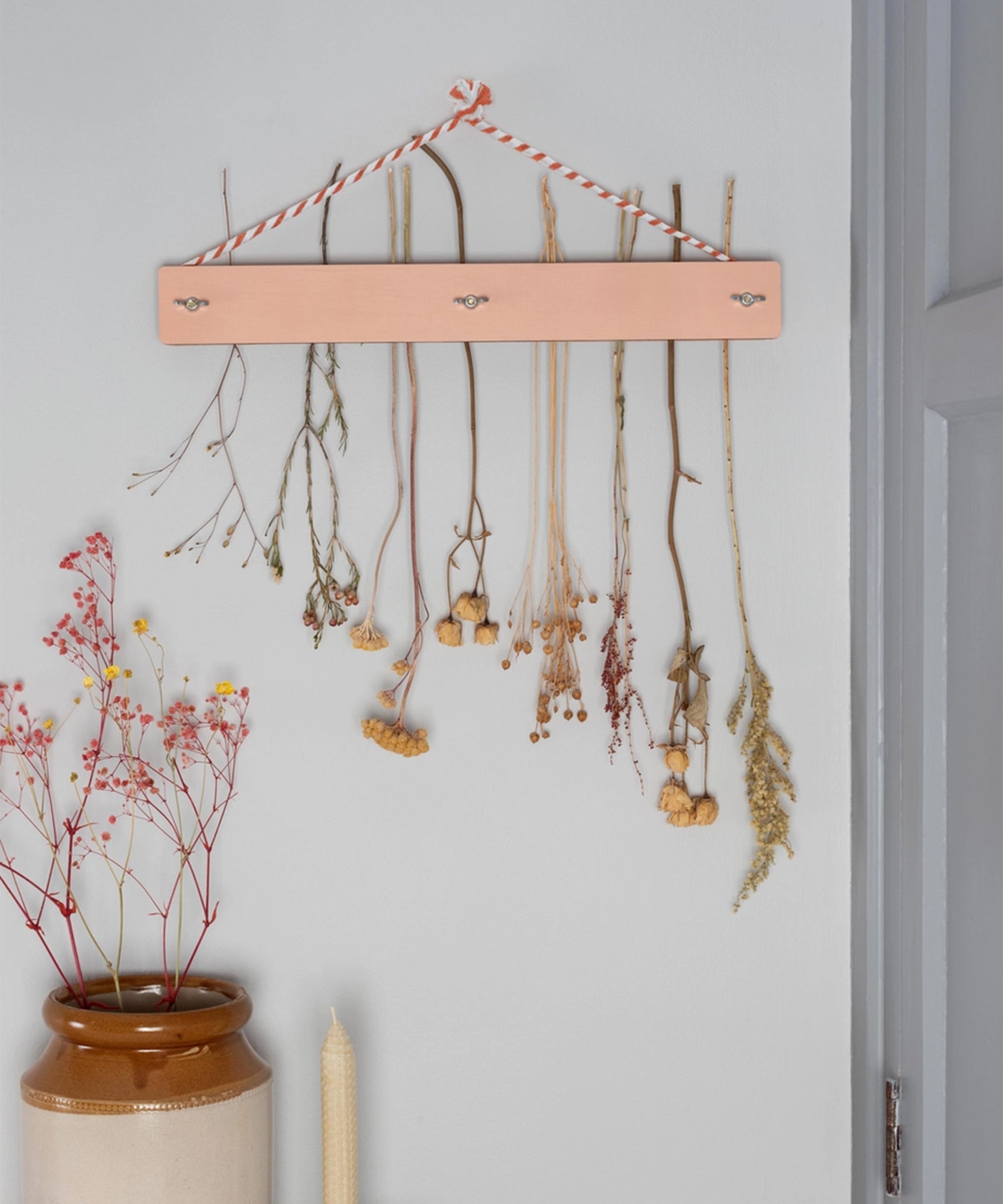 A Flower Drying Kit hangs on the wall above a vase filled with dried flowers.