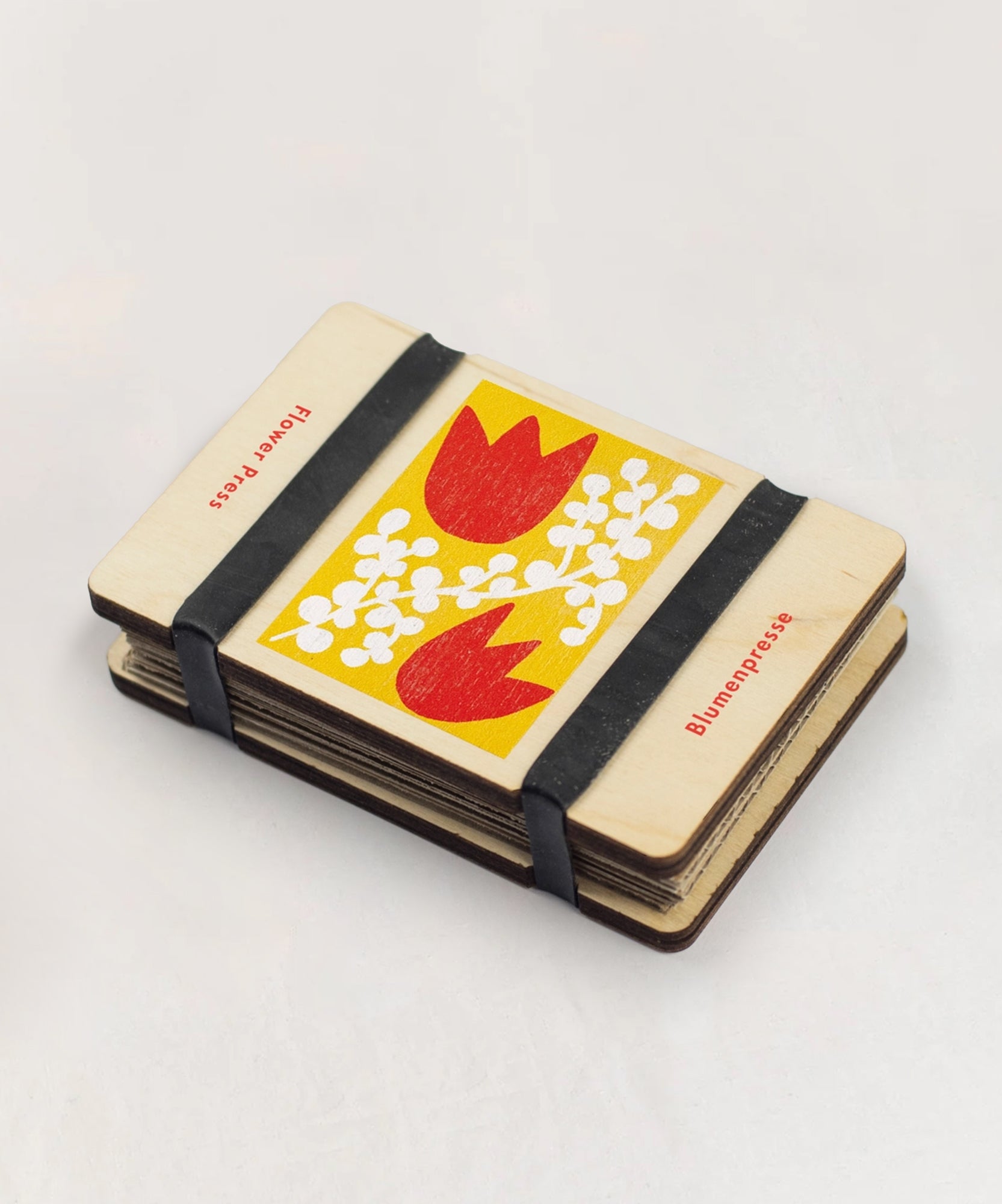 The Pocket Flower Press is a small wooden press with red tulip and white floral designs, secured by black straps.