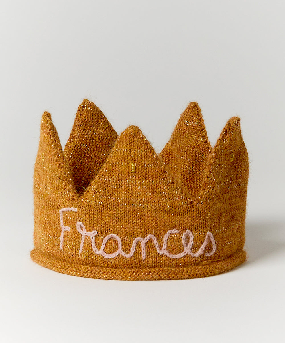 A knitted light pink crown with "Gold" personalized on the front.