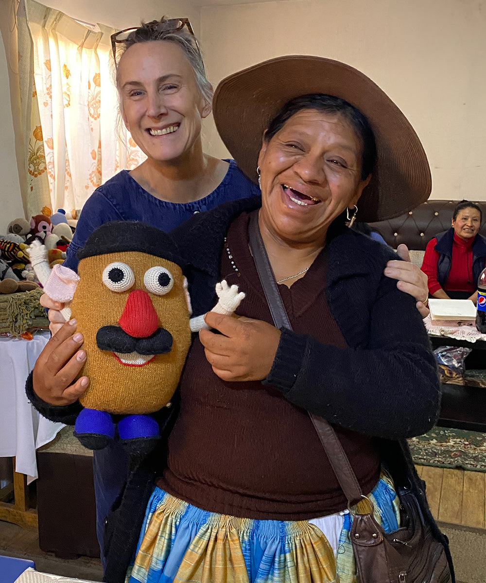 Two women smiling, holding a Funny Face Pillow, in a warmly lit indoor setting.