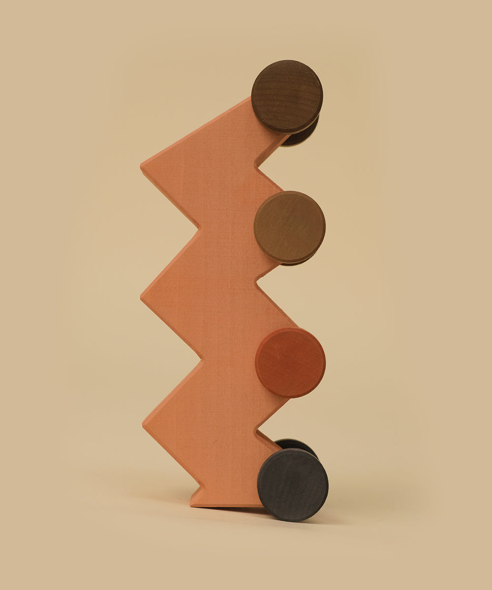 Le Zigzag Vehicle is a wooden block standing upright with four round, colorful discs attached along its side.