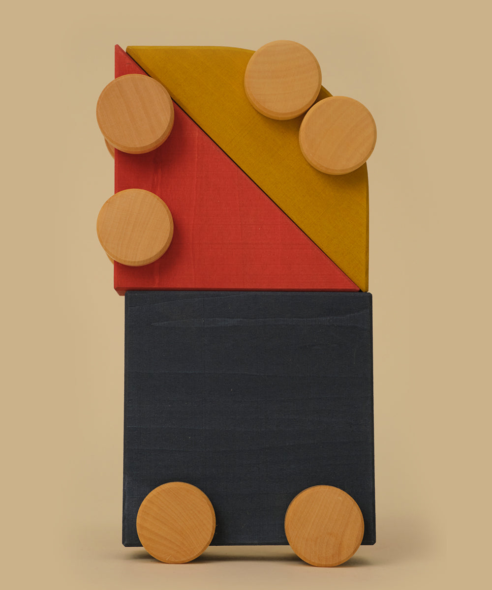 Le Vehicle Trio features stacked colorful wooden blocks with six round wooden discs arranged on top and sides, set against a beige background.