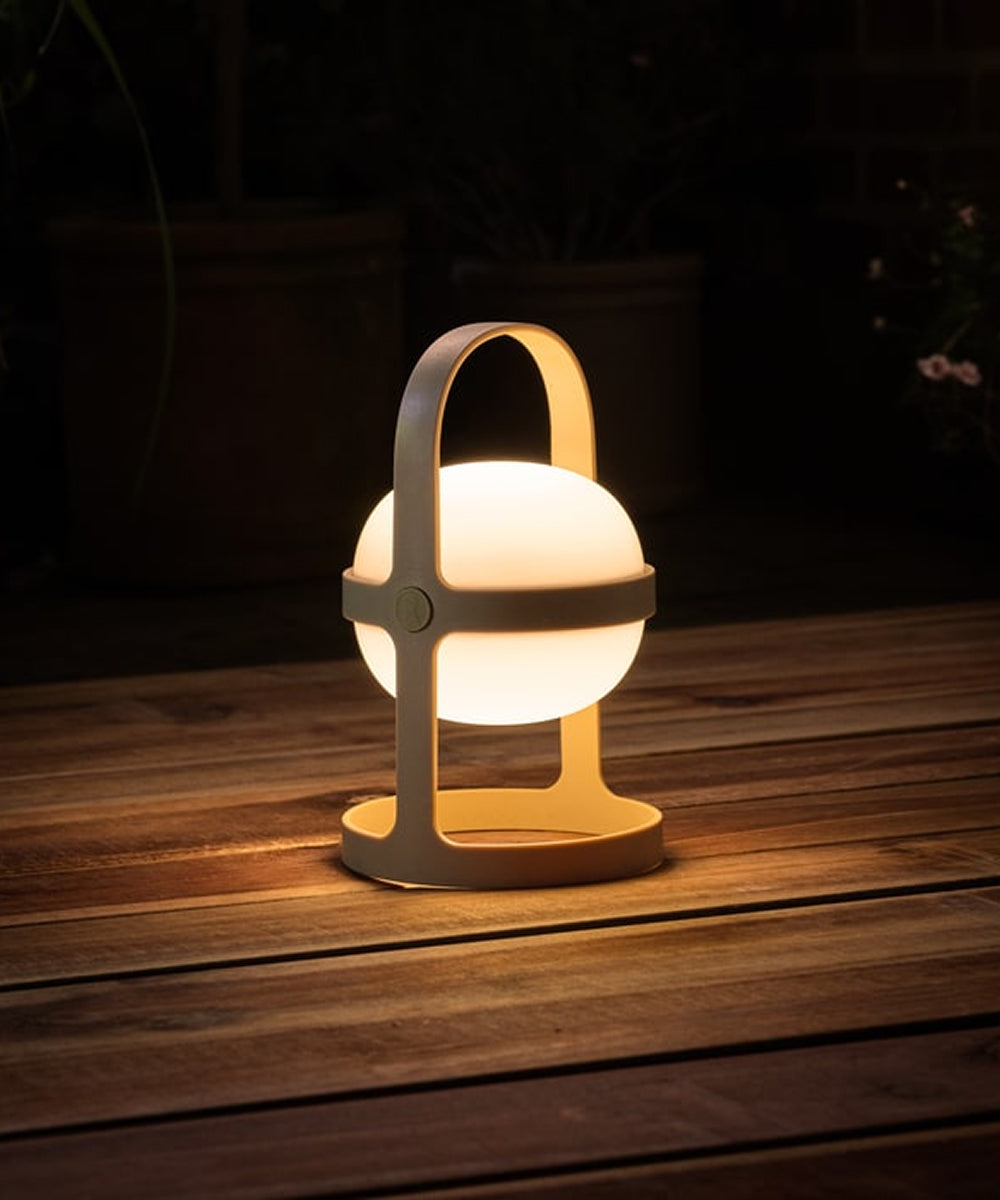 The Rosendahl Soft Spot Solar Circular in Wheat emits warm light, resting on wooden floorboards in a cozy, dark space.