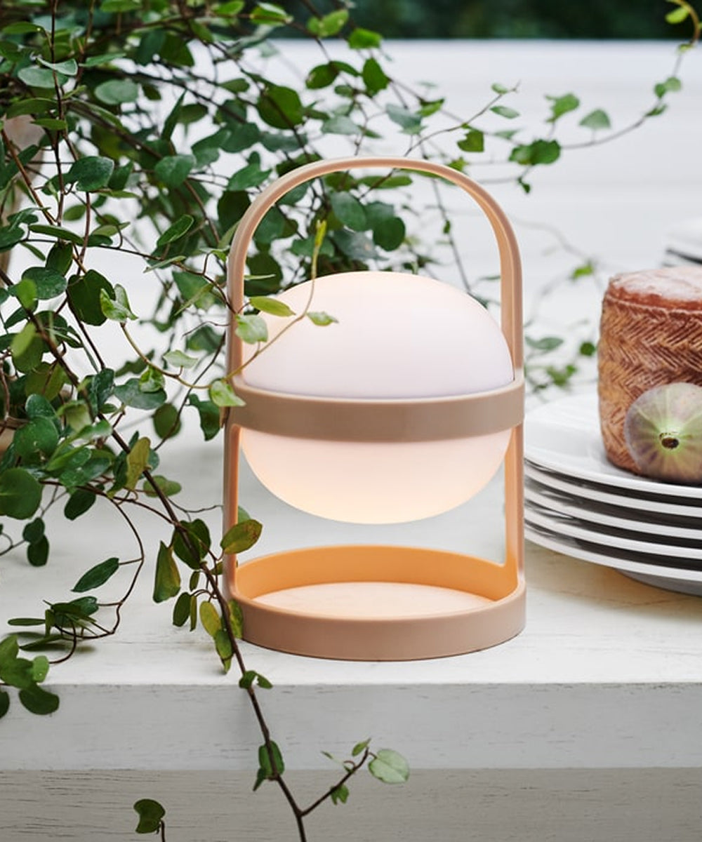 The Rosendahl Soft Spot Solar Circular, Wheat, with its beige handle, rests on a white table by green vines, plates, and wrapped cheese.