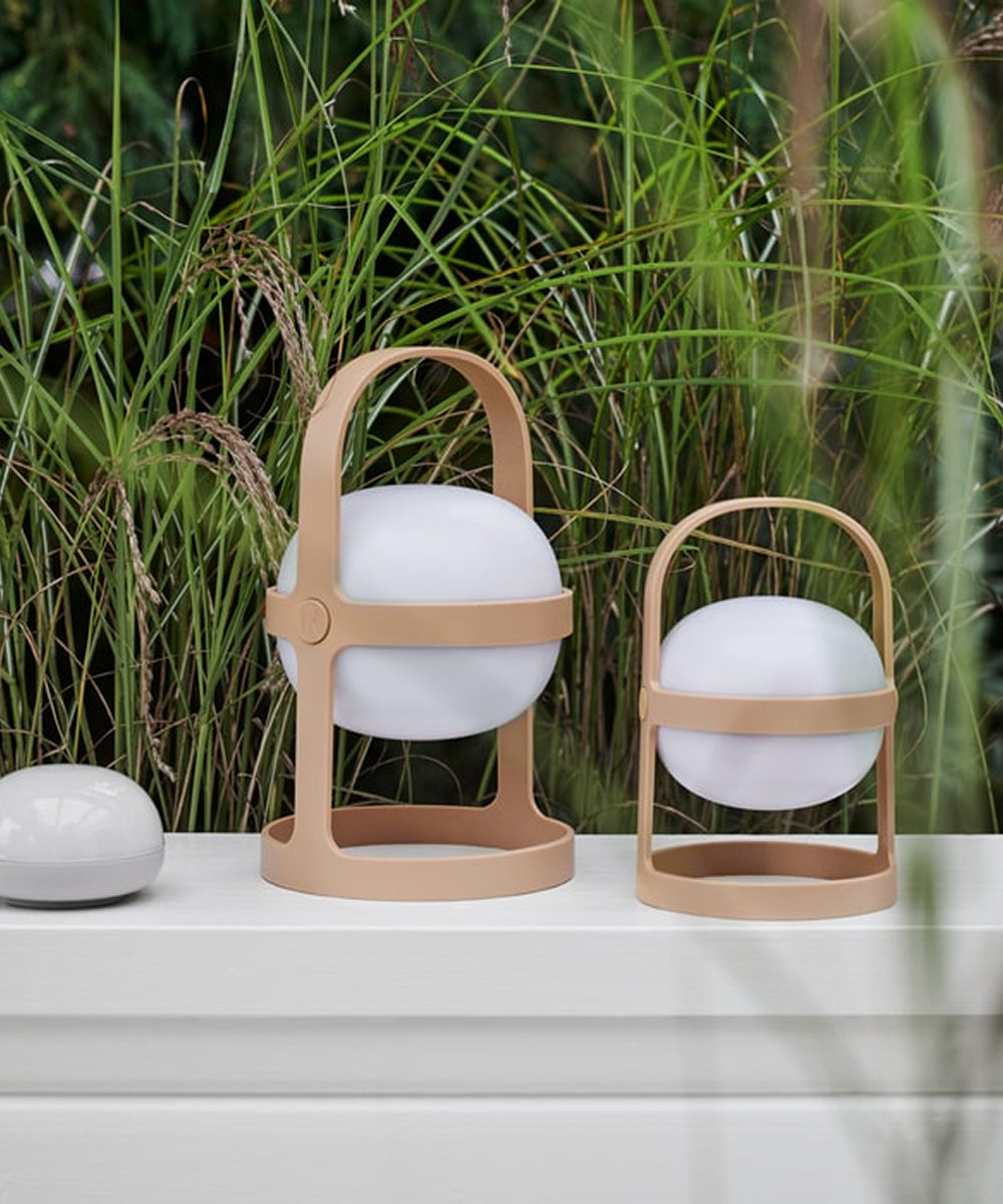 Two Rosendahl Soft Spot Solar Circular lanterns in Wheat sit on a white surface outdoors, surrounded by tall green grass.