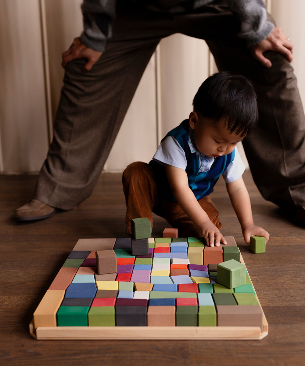 A young child sits on the floor, playing with colorful Le Oddy Cubes blocks on a tray.