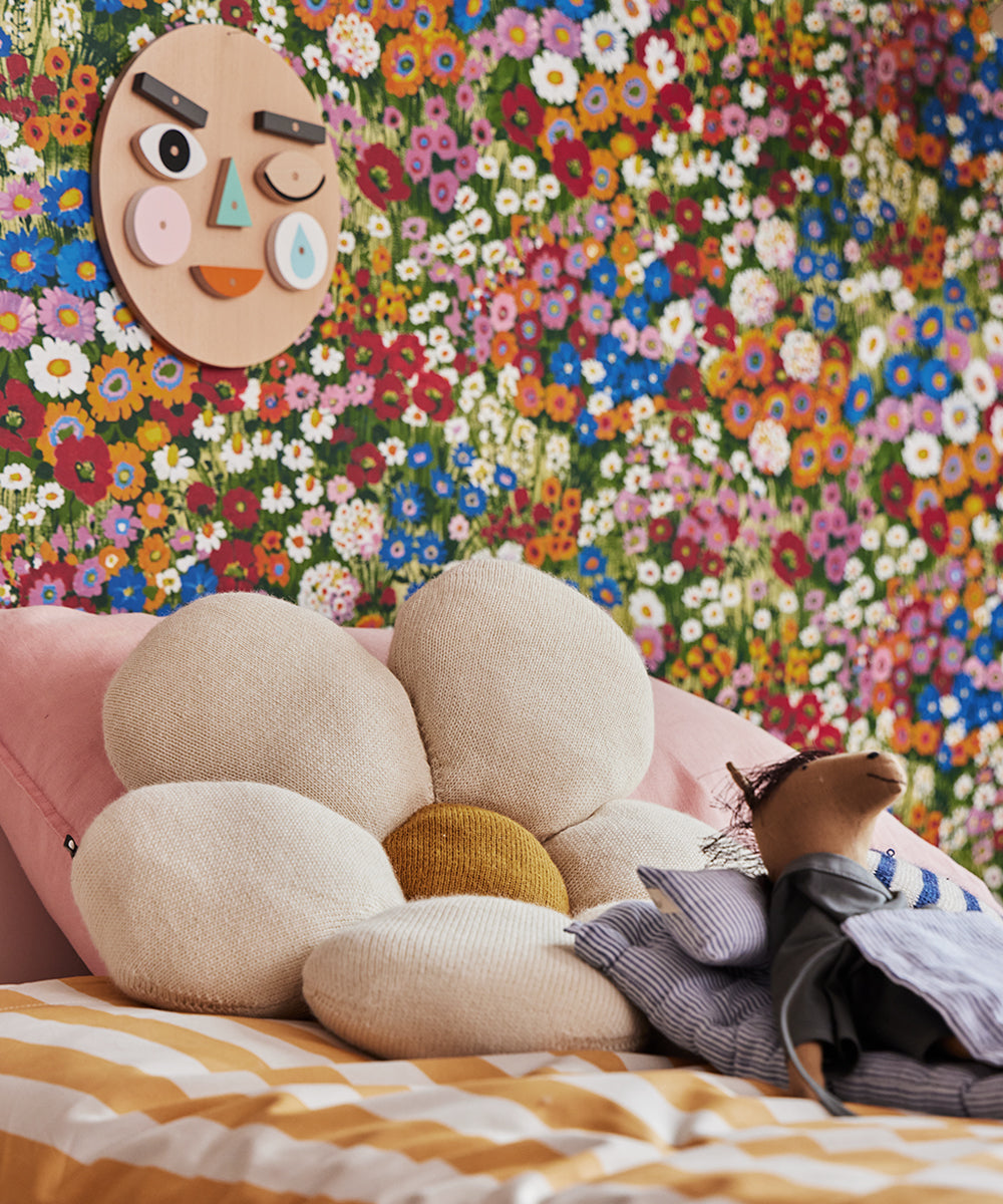 The Le Horsey bed features a large flower-shaped cushion and a stuffed bear dressed as a scarecrow, complemented by colorful floral wallpaper and a wooden face art piece on the wall.