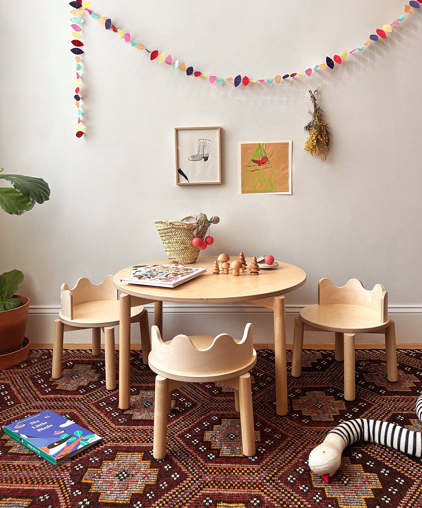 Children's playroom with a round table, Moss Chairs (Set of 2), colorful books, and decorations on a patterned rug.