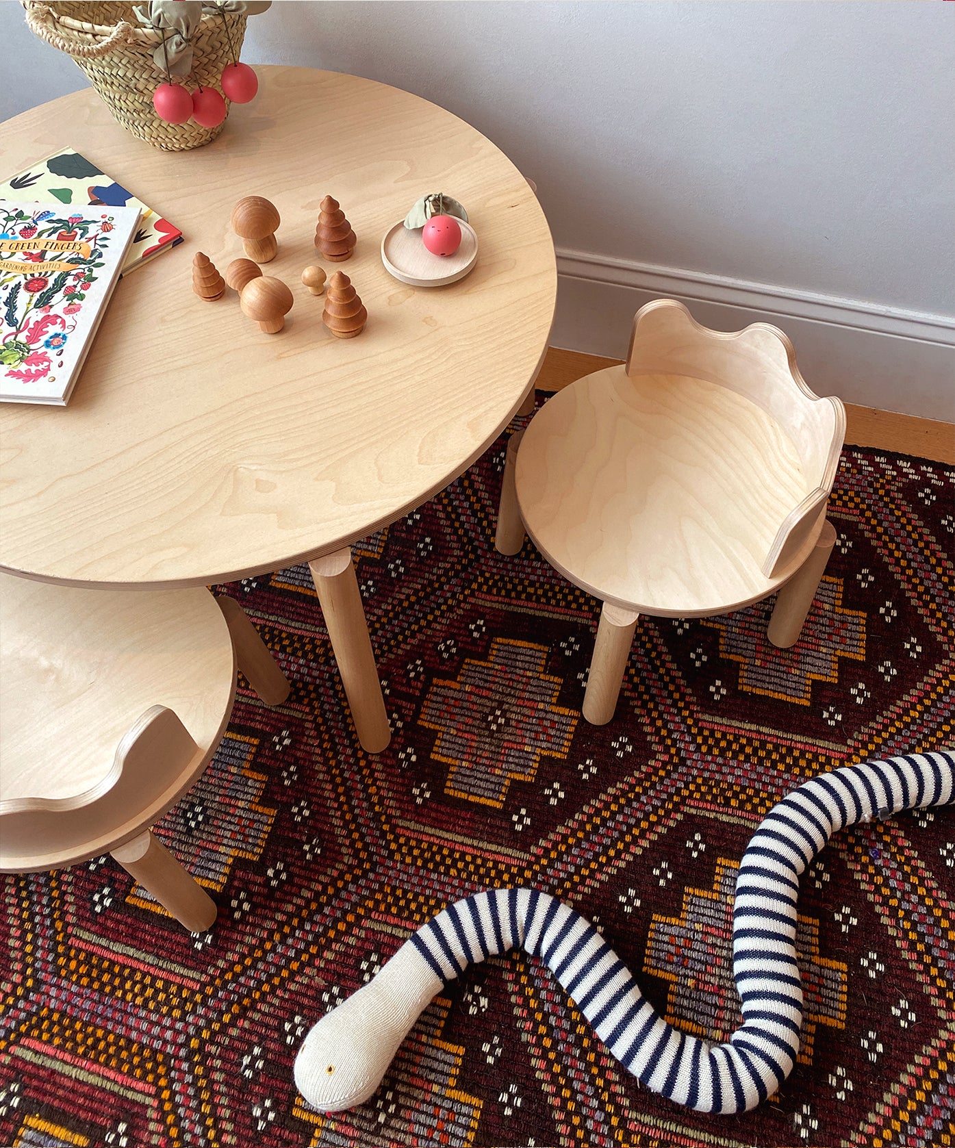 A play area featuring Moss Chairs, a toy snake on a patterned rug, and wooden toys on a round table.