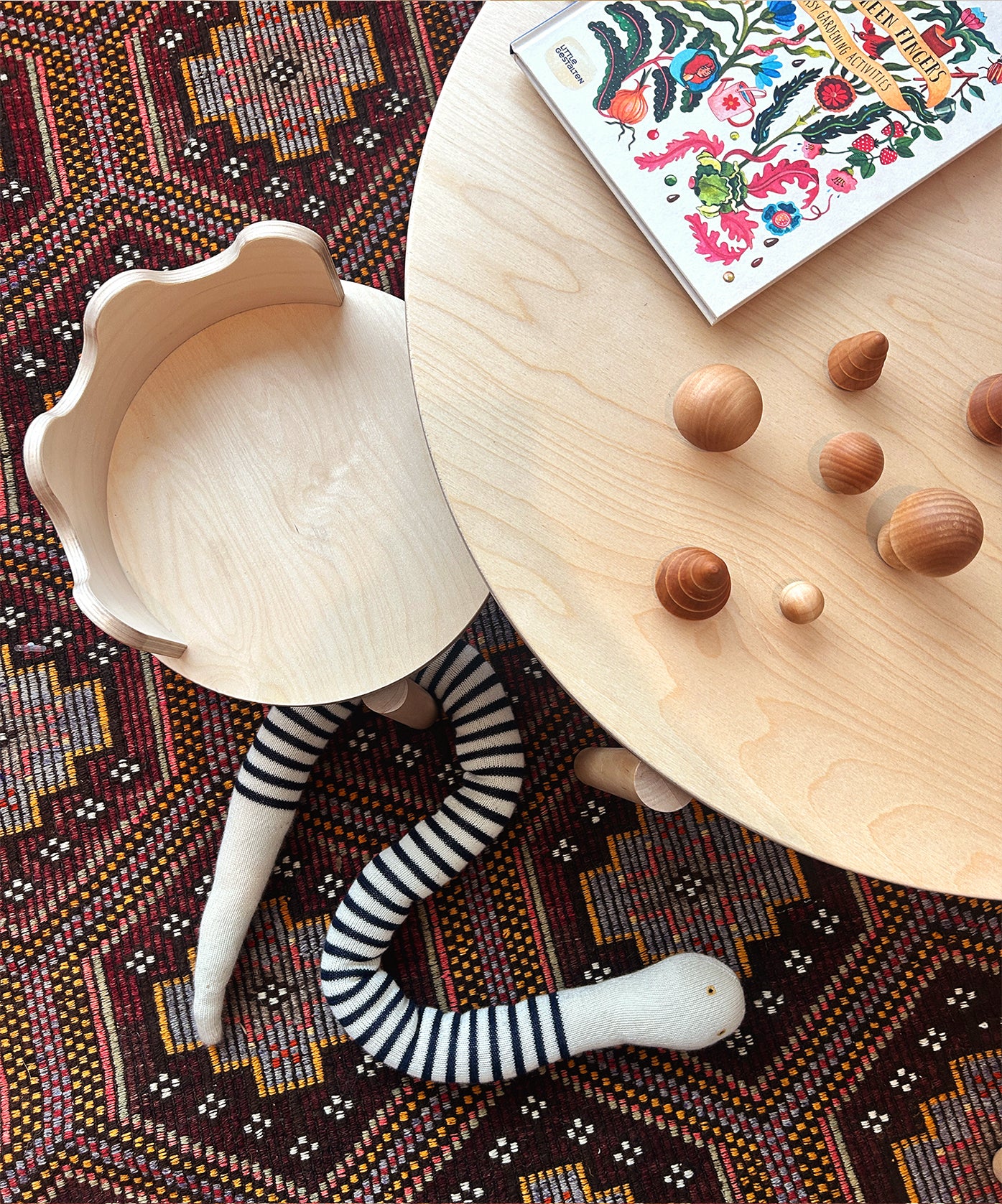 Moss chairs, a striped snake toy, a book, and wooden acorns on a patterned rug.