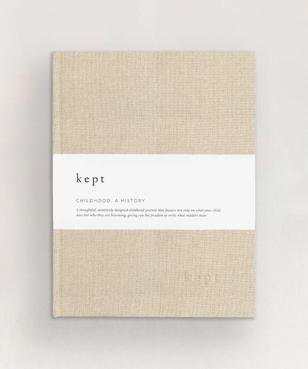 A beige textured journal named "Le Baby Book," wrapped in a white band with descriptive text.