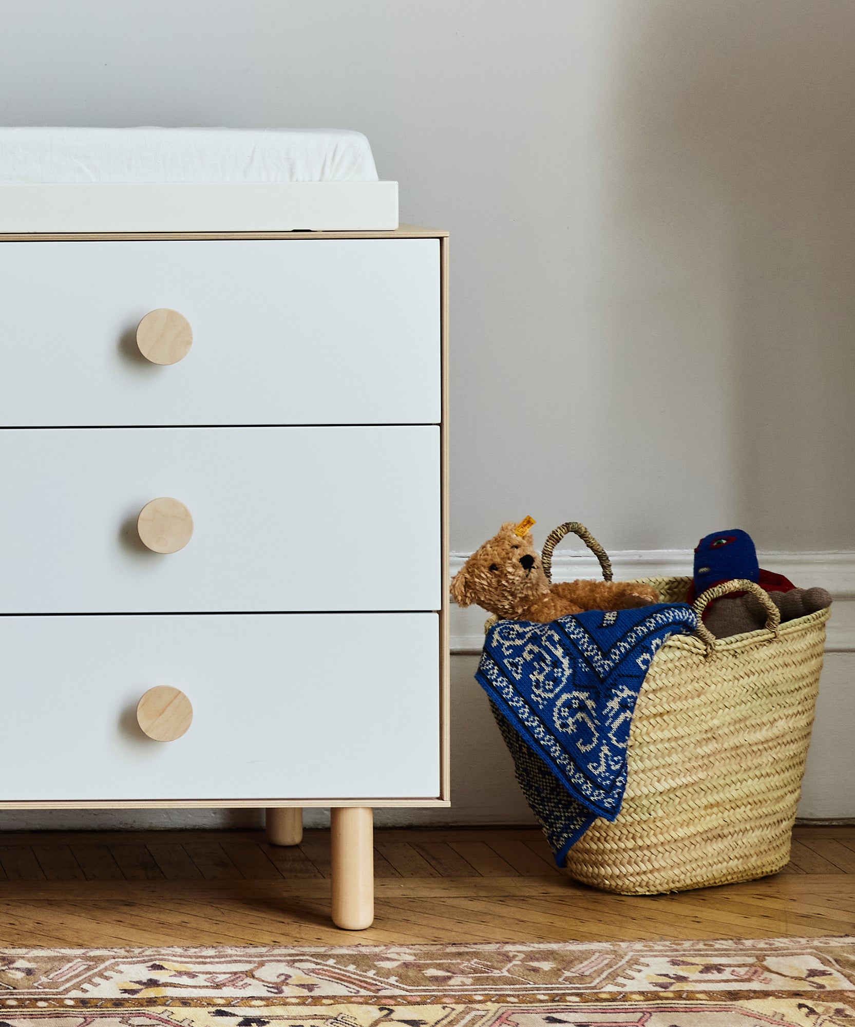 White dresser with large round knobs next to a Le Market Basket - Large, holding toys and a blue patterned cloth.