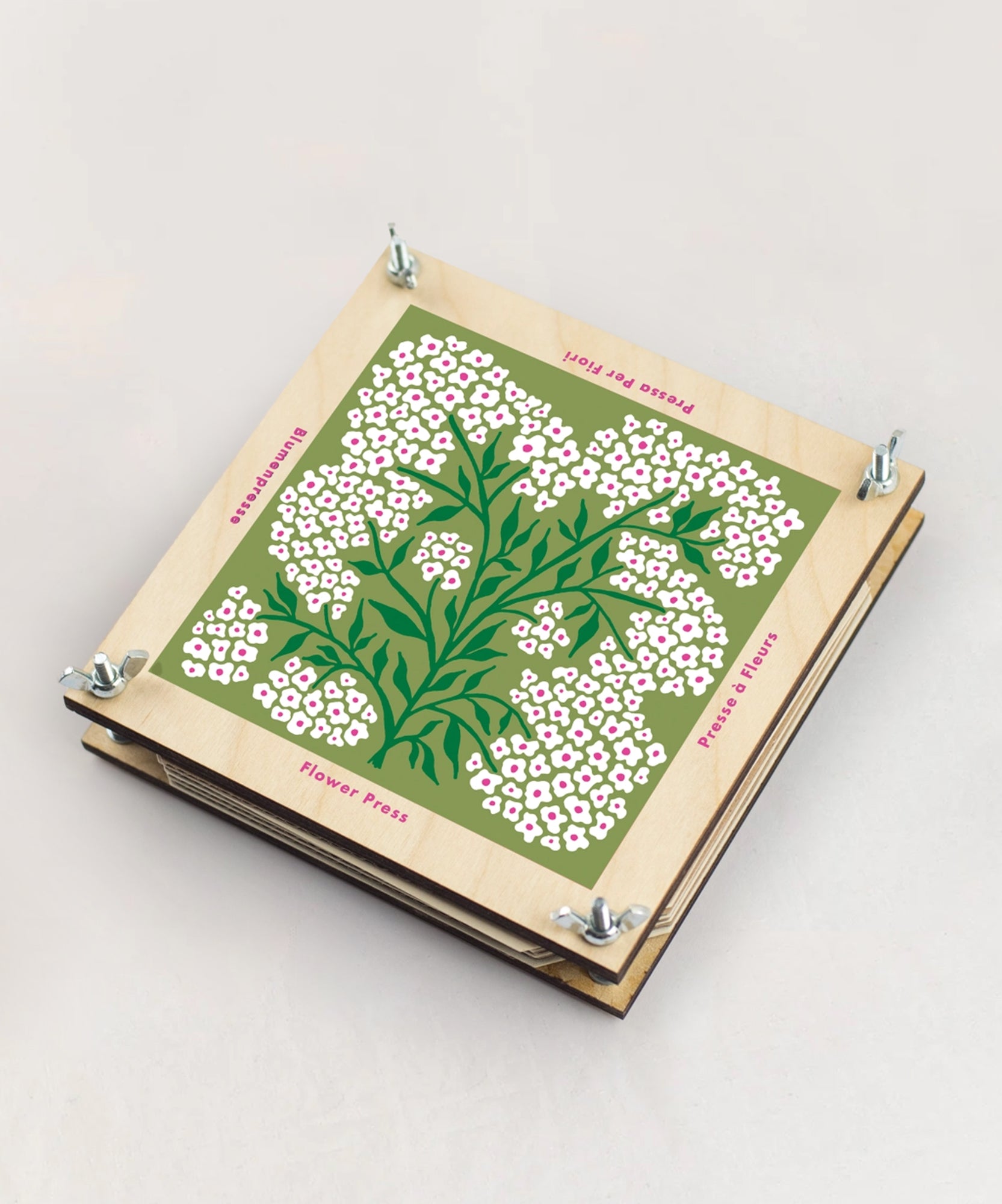 A Flower Press featuring a floral illustration and metal bolts at each corner rests on a light surface.