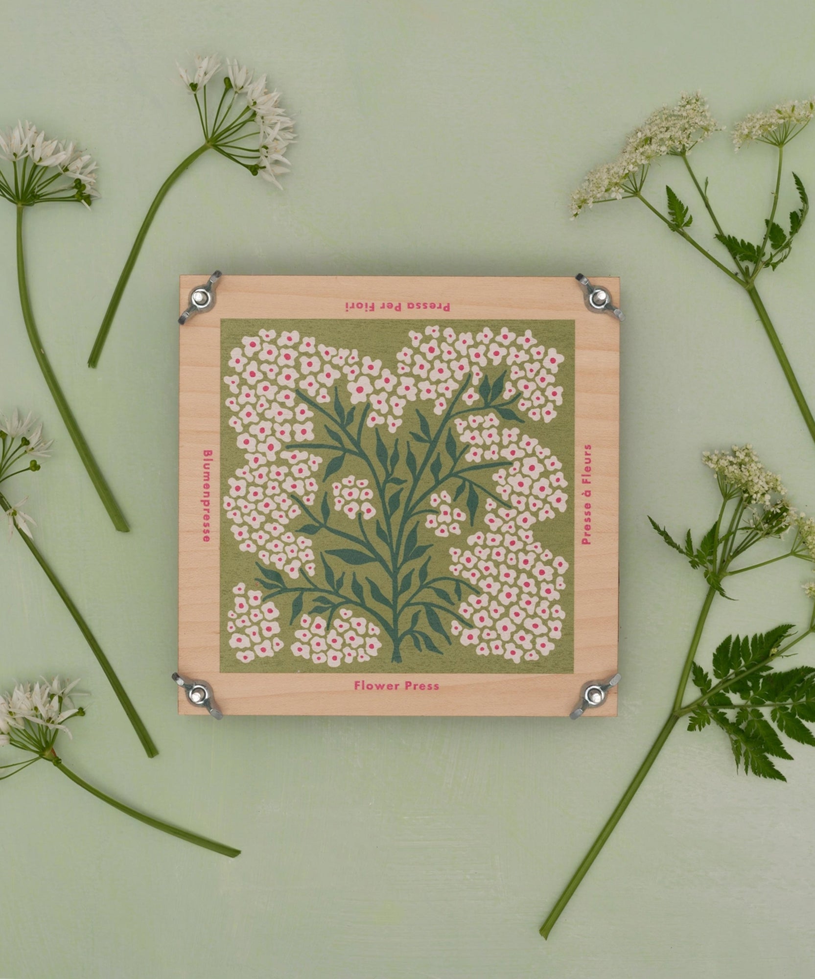 The Flower Press features a wooden design with floral patterns, displayed among small white flowers on a pale green background.
