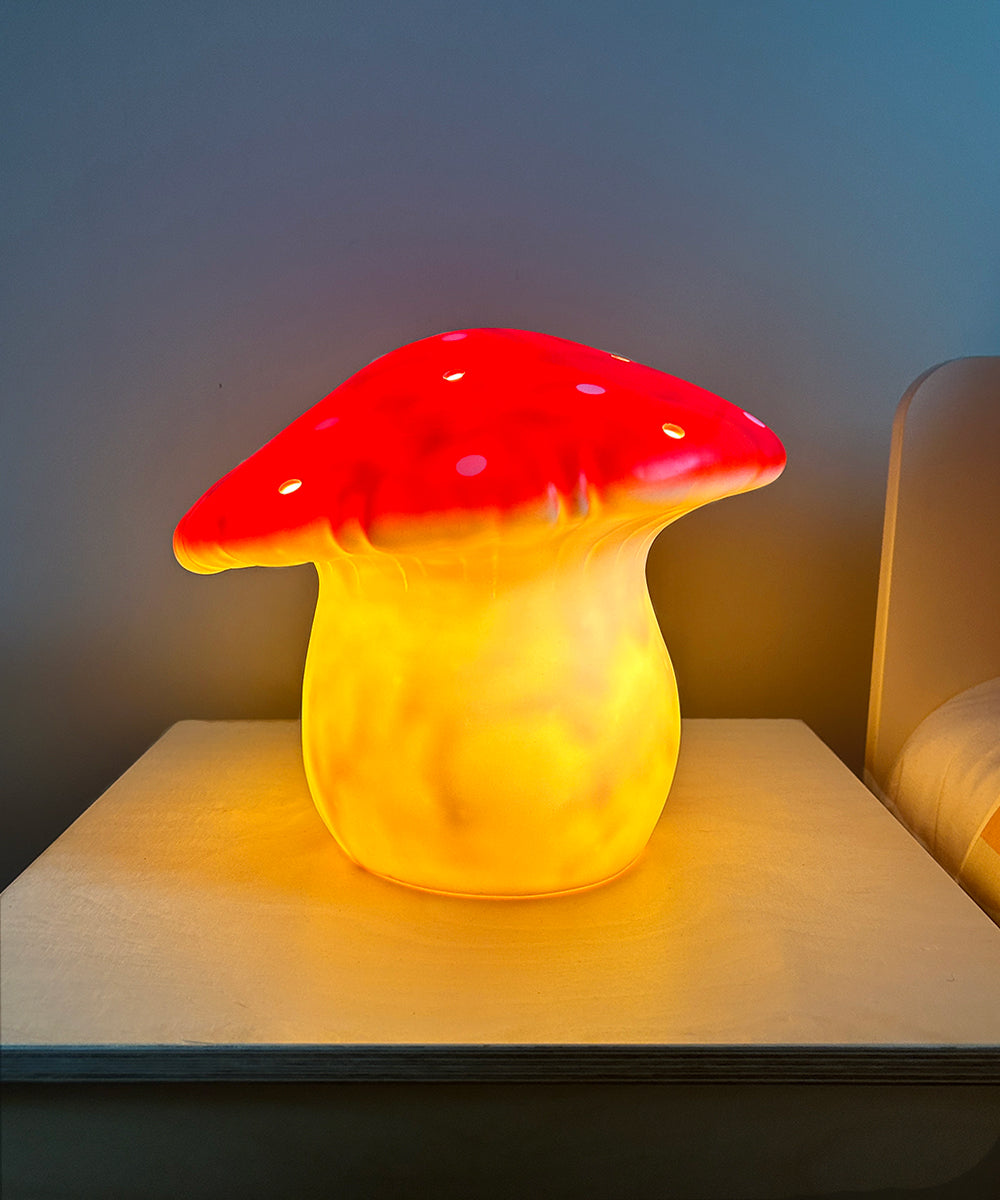 Le Big Mushroom Lamp, with its glowing yellow base and red cap, sits elegantly on a bedside table.