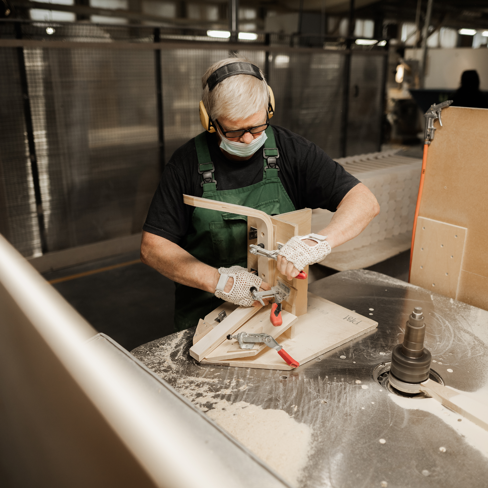 Person wearing safety gear operates a woodworking machine in a workshop, handling wood with precision.