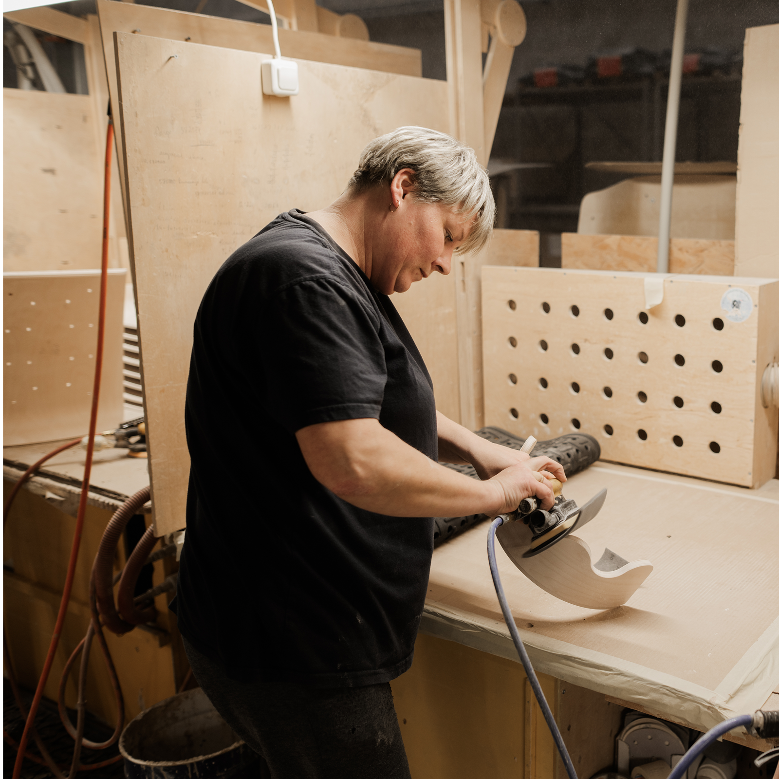 Person using a power tool to shape a wooden object on a workbench in a workshop.