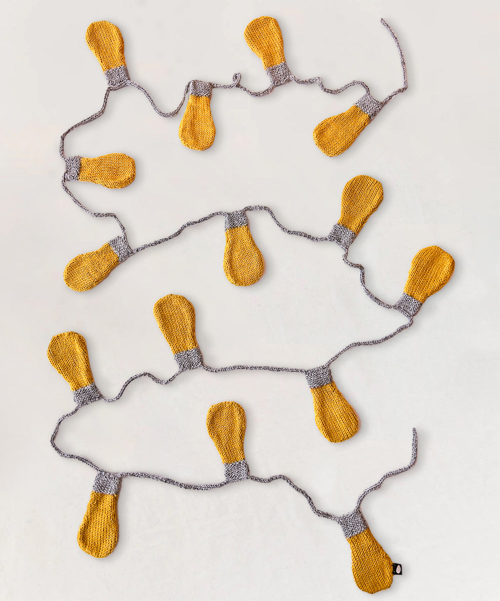 The Light Bulb Garland features knitted yellow bulbs on a gray string, beautifully arranged on a white surface.