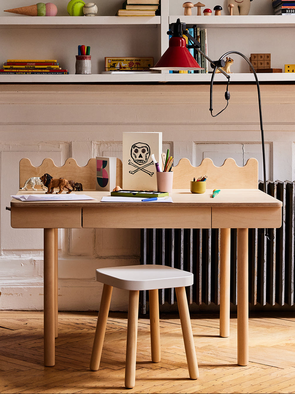 A kids’ wooden desk with art supplies, animal figures, a skull drawing on top, and a Square Stool.