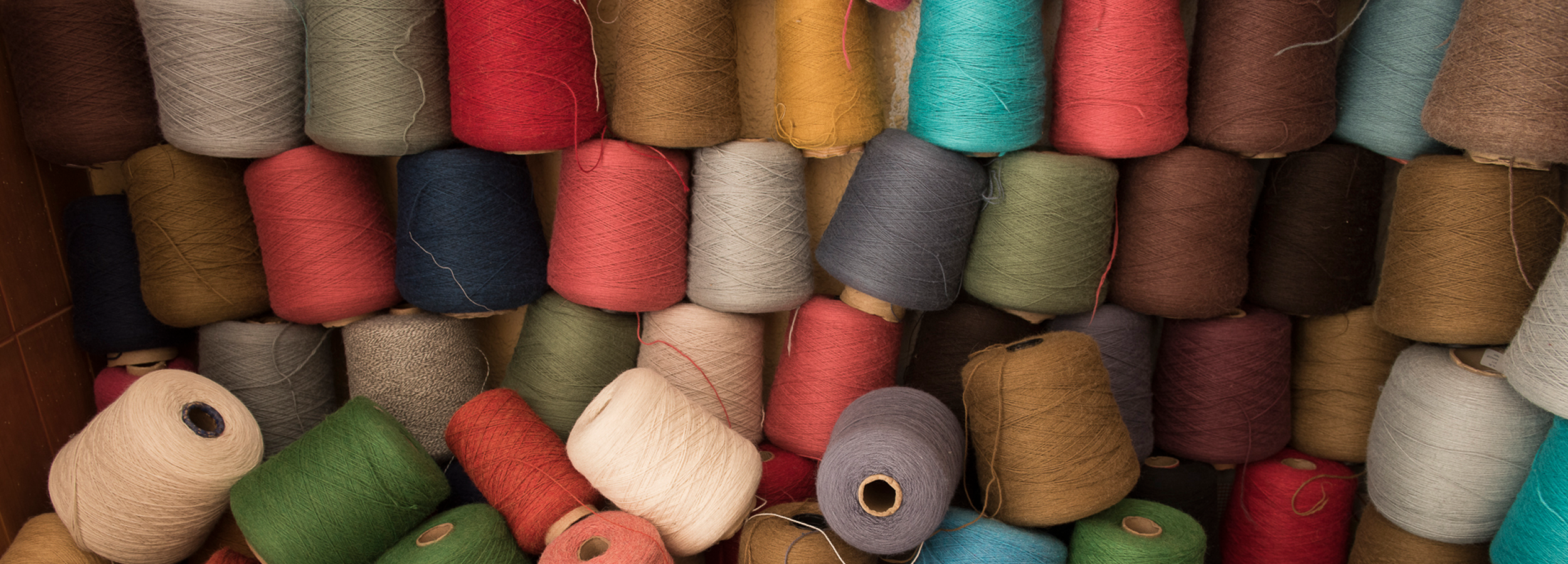 Stacks of colorful yarn spools in various shades, arranged vertically and horizontally.