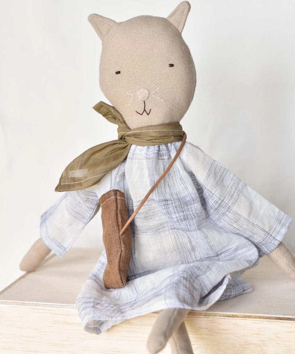 Mae le Cat, a stuffed cat doll in a plaid dress and scarf, sits on a wooden surface.