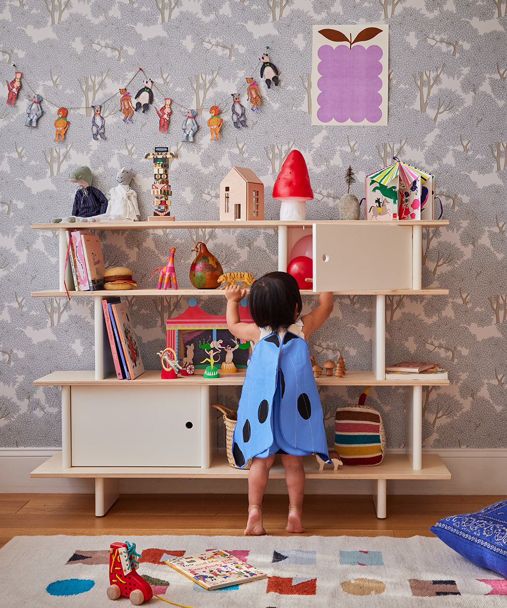 A toddler in a blue outfit plays with toys near the Le Small Mushroom Lamp on a shelf in a colorful room with patterned wallpaper.