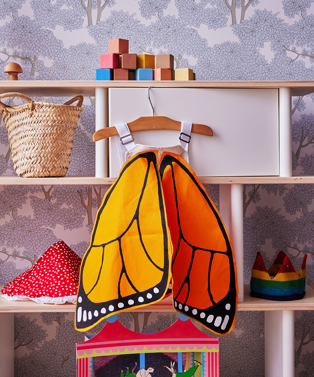 Children's room featuring Le Monarch Butterfly Wings on a hanger, wooden blocks, baskets, and decorative hats on shelves.