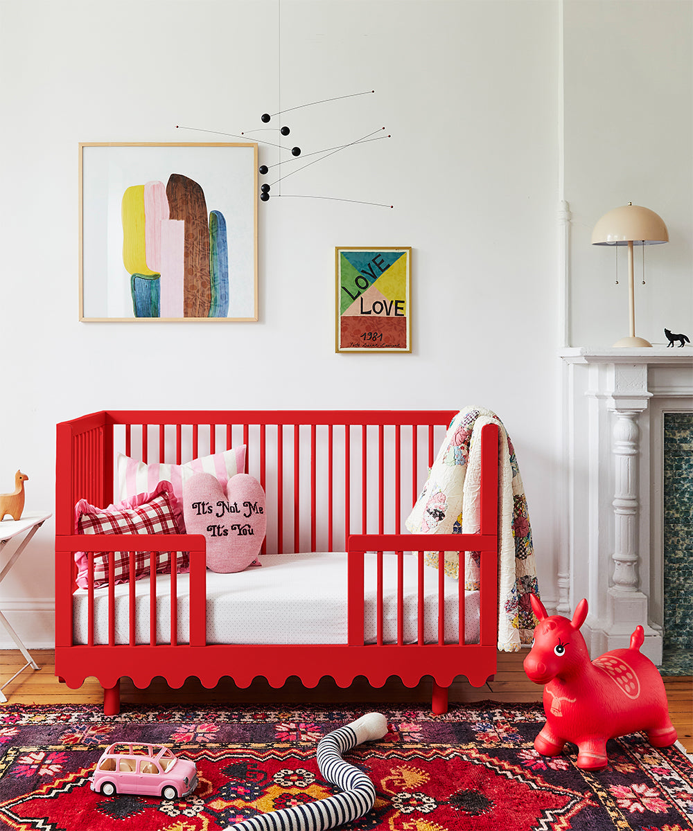 A colorful nursery featuring a vibrant Moss crib, lively wall art, a patterned rug, and toys scattered across the floor.