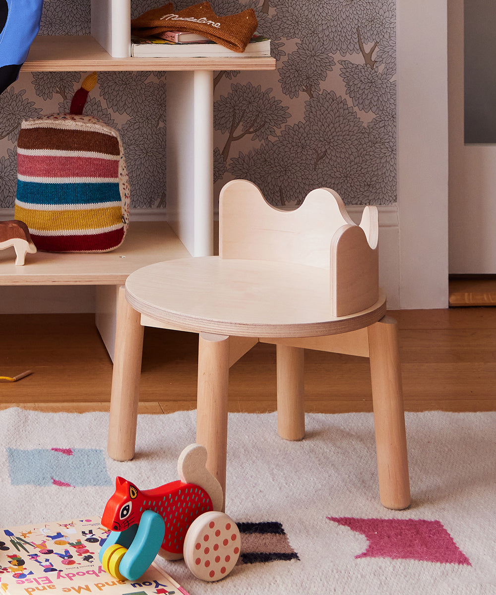 A Moss Chair sits in a children's room, surrounded by books and a red wooden toy scattered on the floor.