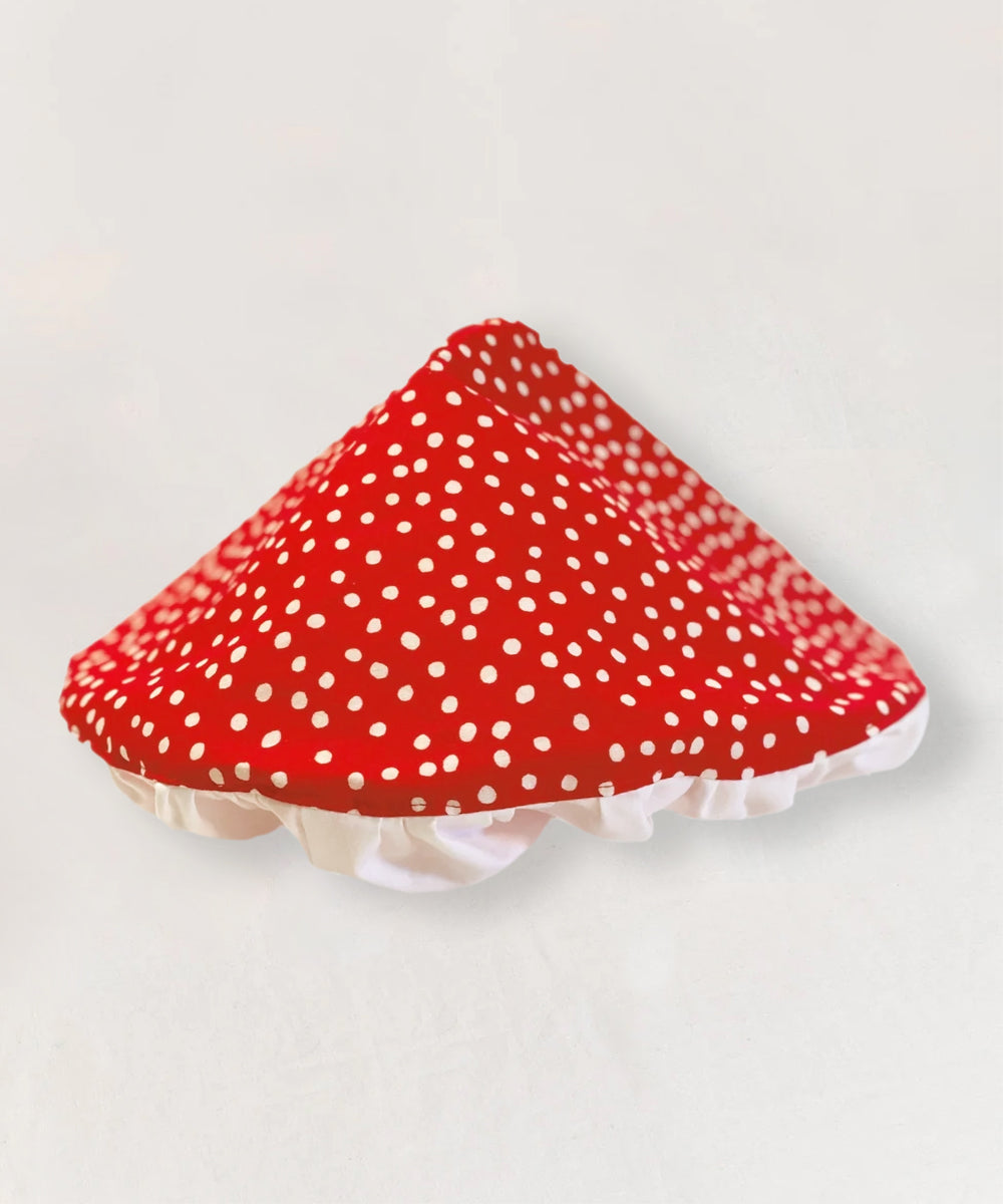 Le Mushroom Hat is a red triangle-shaped hat with white polka dots and a frilled white trim, inspired by a mushroom cap.