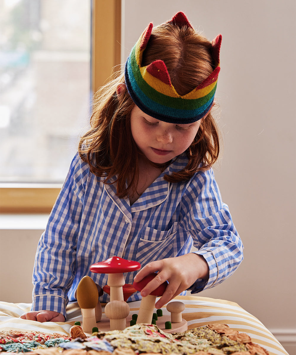 A child wearing a rainbow crown and striped pajamas plays with the Le Mushroom Sorter on a bed.