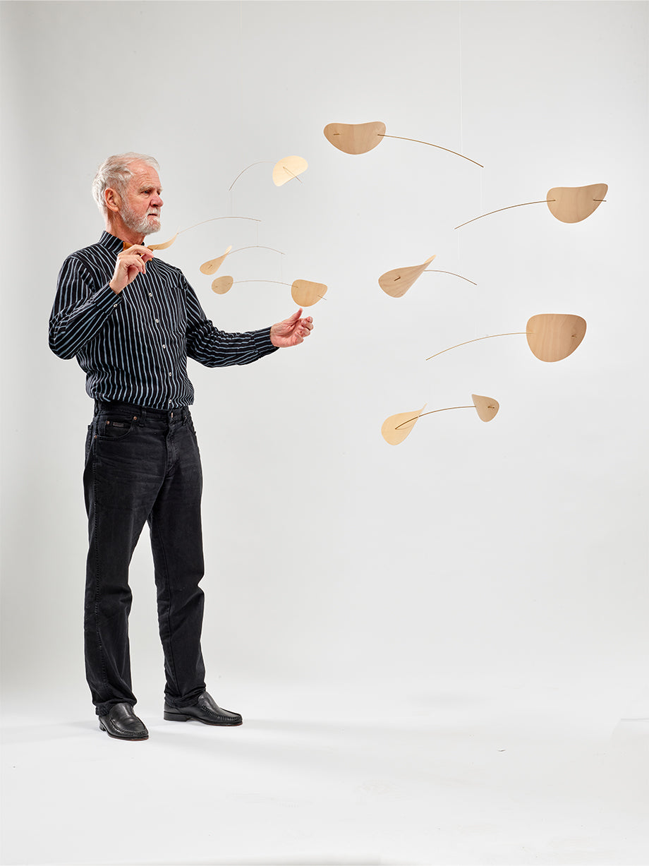 An older man adjusts the Drifting Clouds | Nature | Size M wooden mobile with leaf-shaped pieces against a plain white background.