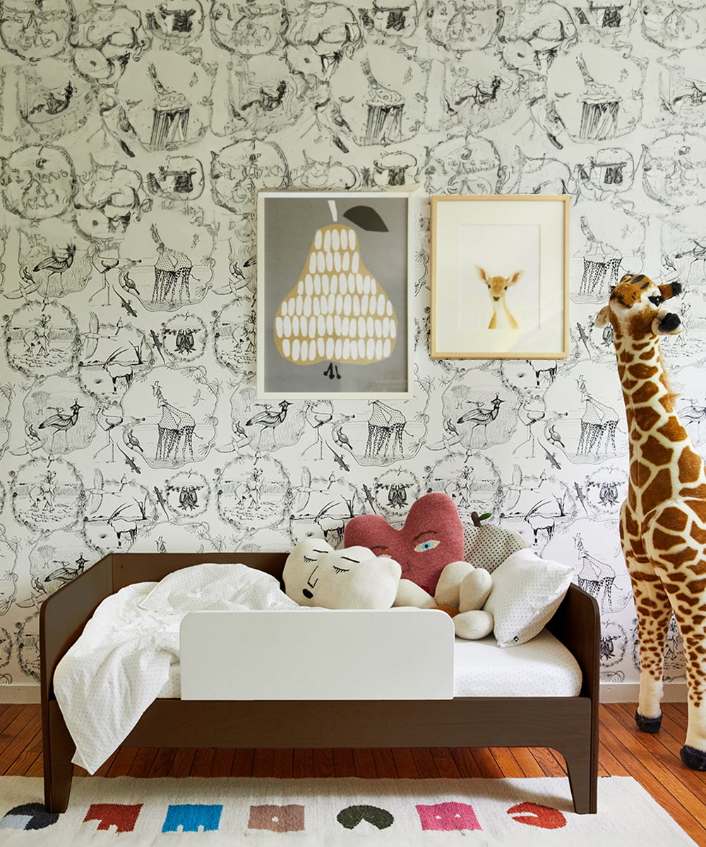 A childrens room features a Perch Toddler Bed, a variety of plush toys, a giraffe statue, and animal-themed illustrated wallpaper.