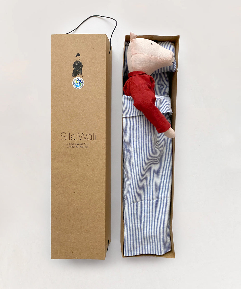 A doll named "Le Piggy" with a red shirt lies in a cardboard box beside packaging marked "SilaiWali.