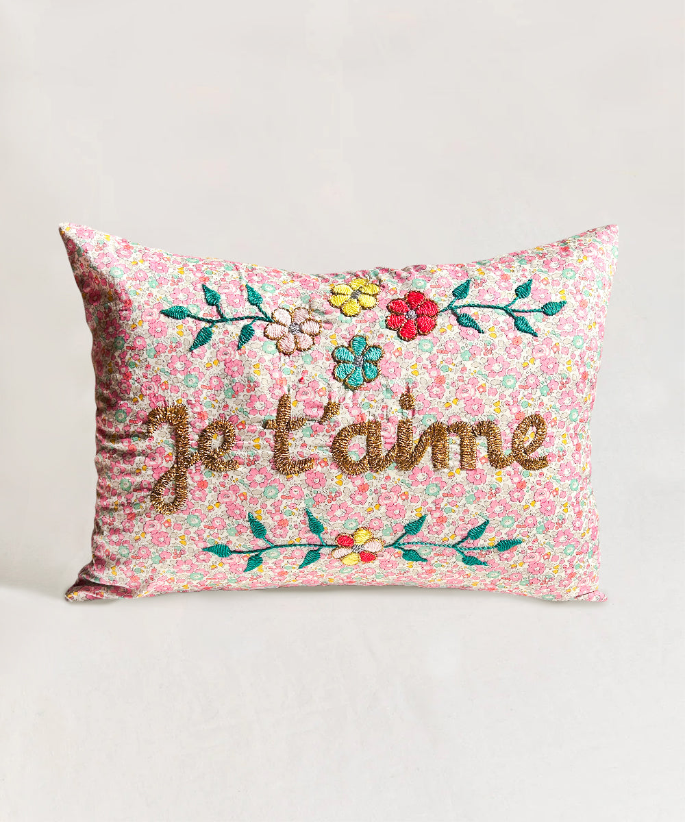Le Embroidered Pillow - Je T'aime: Rectangular pillow featuring colorful floral print and gold "je t'aime" embroidery, with flowers above and below the text.