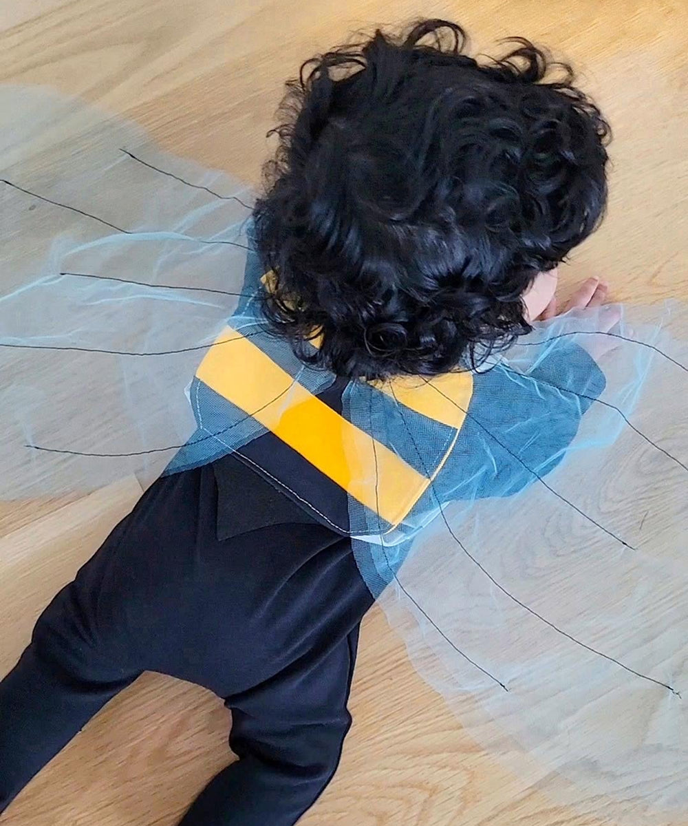 A curly-haired child wearing Bumble Bee Costume Wings crawls on a wooden floor.