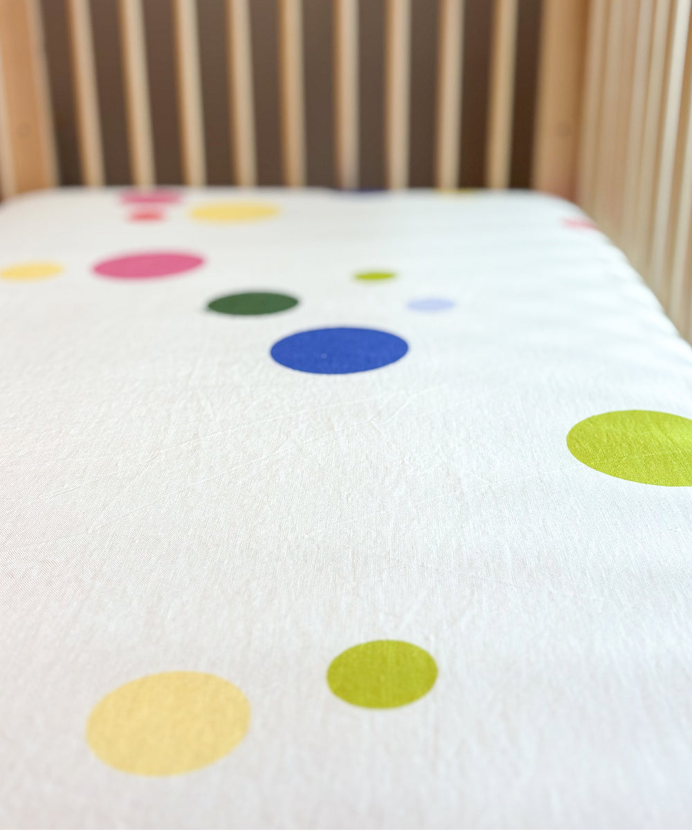 Printed Linen Crib Sheet in white with scattered multicolored polka dots.