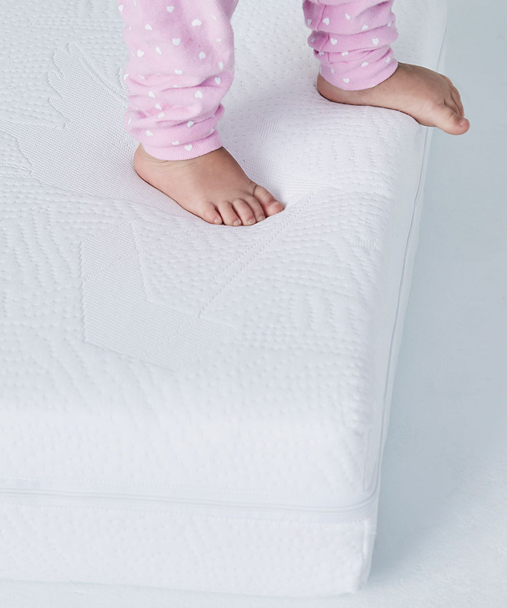 A child's bare feet on a Dual Firm Crib Mattress; the child is wearing pink pants with tiny white hearts.