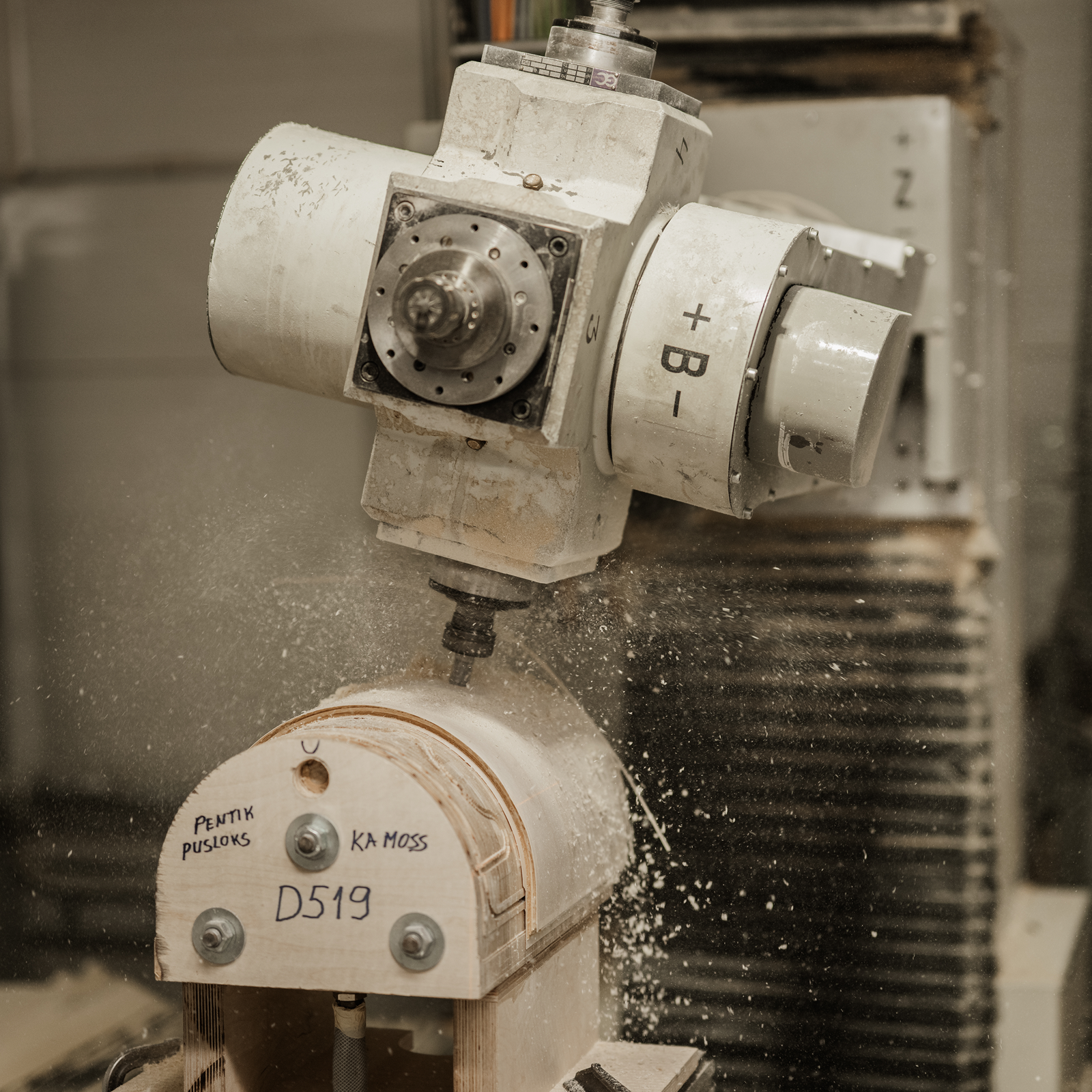 A CNC machine in operation, cutting a curved piece of wood labeled D519, with sawdust visible in the air.